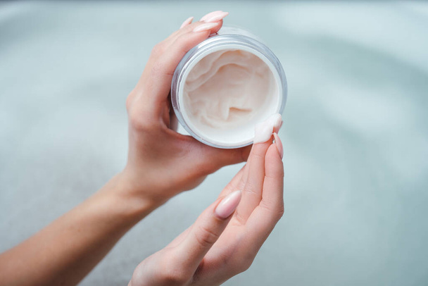 Top view of a pink cream or face mask in the hands of a girl. A woman holds a jar of cream on the background of foam in the bath. Spa procedure, body care, skin health product - Foto, immagini