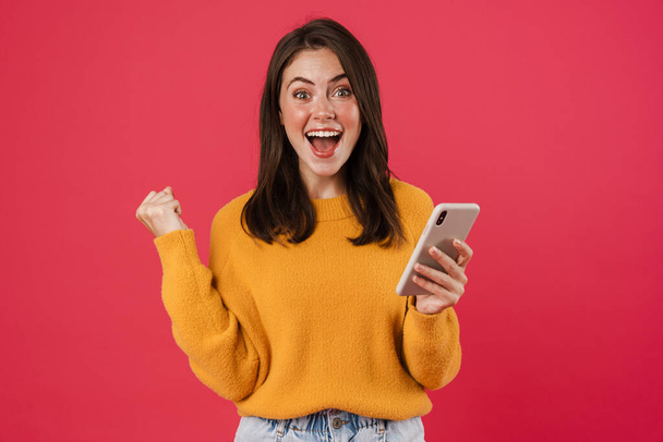 Excited young woman holding mobile phone, celebrating isolated over pink background - Fotó, kép