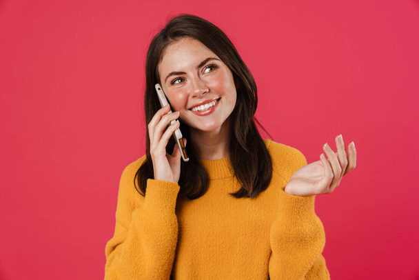 Kuva iloinen brunette tyttö hymyilee ja puhuu matkapuhelin eristetty vaaleanpunainen tausta - Valokuva, kuva