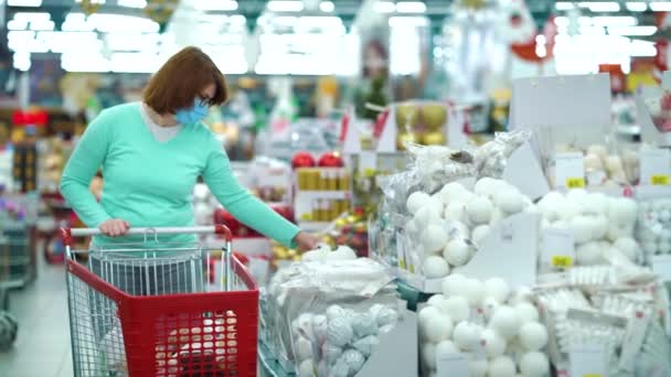 Woman in medical mask buying Christmas decorations in supermarket - Filmagem, Vídeo