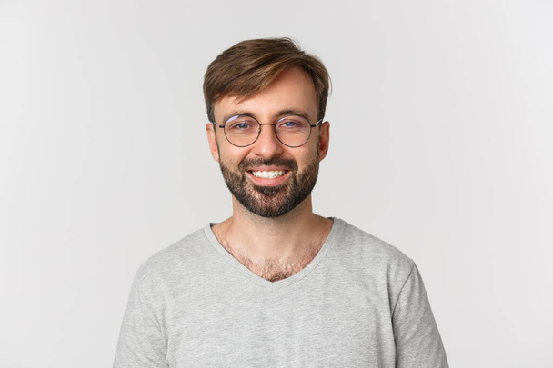 Close-up of handsome modern guy in glasses, smiling and looking at camera, standing over white background - Φωτογραφία, εικόνα