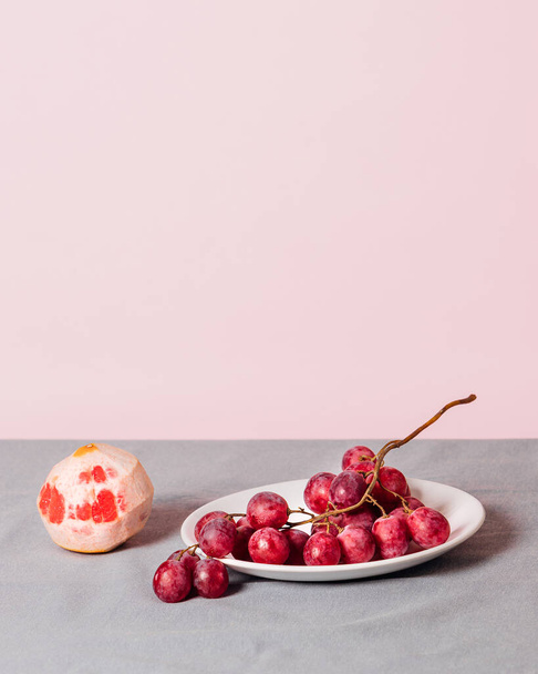 Close-up of a bunch of grapes and a peeled grapefruit on a pink background. Minimalist still life with copy space for your text. - 写真・画像
