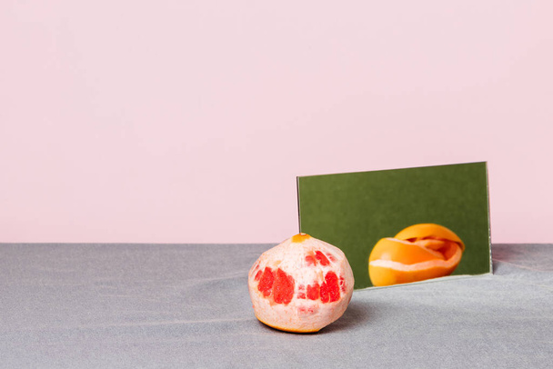 Stillleben einer geschälten Grapefruit, deren Schale sich auf einem Spiegel auf rosa Hintergrund spiegelt. Ernährungskonzept. - Foto, Bild