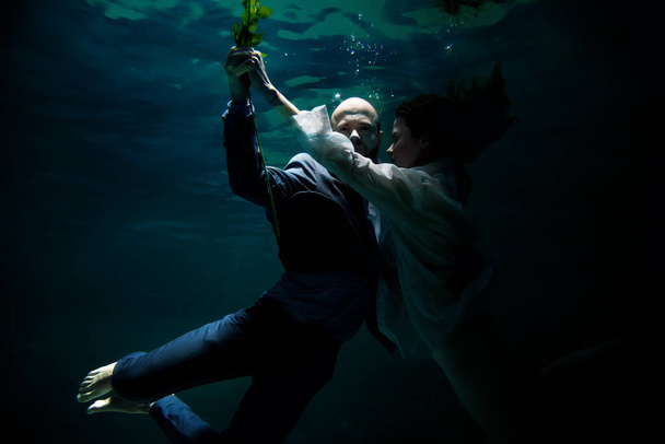 Young businessman dancing with his woman, symbolizing success, win, underwater. Emotional happy couple in pond. Concept romantic date and commitment to development of relations. Copy space - 写真・画像