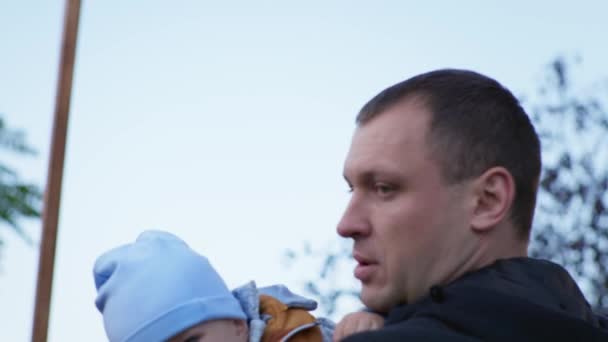 kleine jongen huilt op vaders armen, moeder neemt haar zoon mee om hem te kalmeren tijdens een herfstwandeling in het park - Video