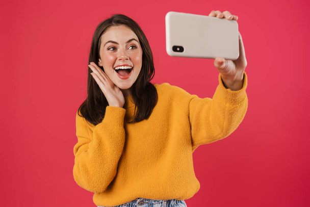 Image of smiling brunette girl taking selfie photo on cellphone isolated over pink background - Foto, Imagem