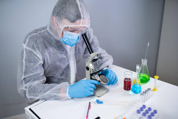 Pharmaceutical manufacturers developing viral medicines by inventing best ingredient. Scientist wearing personal protective equipment with face mask watching cell result under microscope in laboratory - Zdjęcie, obraz