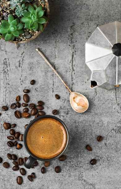 Xícara preta com café expresso, cafeteira e grãos de café em uma mesa de pedra cinza. Top view, coffee or breakfast break - Foto, Imagem