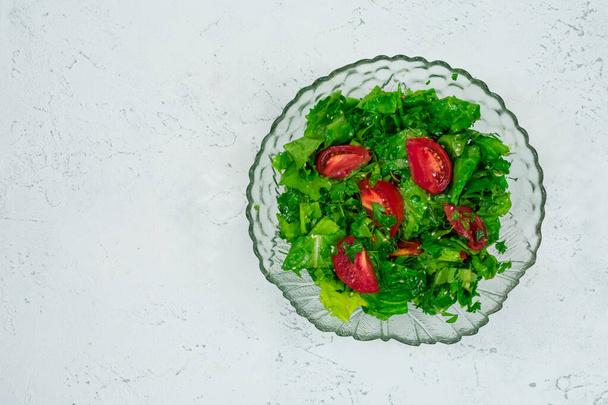 白い石のテーブルの上に緑の葉とトマトの混合物から作られた緑のビーガンサラダ.上からの眺め。碑文の場所. - 写真・画像