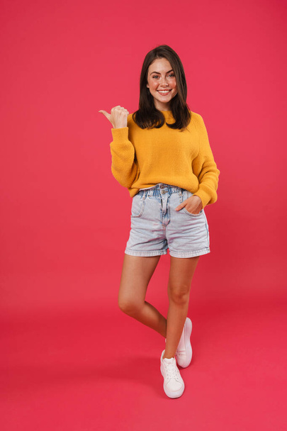 Full length portrait of a happy casual woman pointing finger away isolated on pink background - Foto, immagini