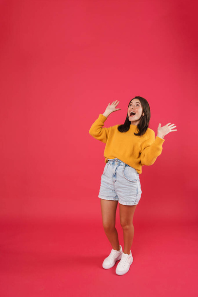 Full length of a happy woman with raised hands trying to catch something falling from the above over pink background - Fotó, kép