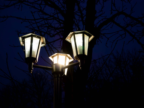 Három hatszögletű utcai lámpa egy oszlopon meleg színt sugároz. - Fotó, kép