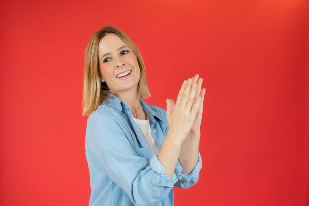 Jonge mooie vrouw voelt zich gelukkig en succesvol, glimlachende en klappende handen, zeggen gefeliciteerd met een applaus tegen de rode muur - Foto, afbeelding