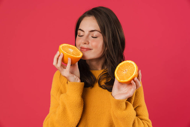 Image of happy caucasian girl smiling while smelling orange isolated over pink background - Fotoğraf, Görsel