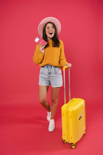 Image of excited caucasian girl posing with suitcase and passport isolated over pink background - Foto, imagen