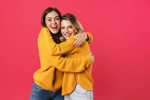 Portrait of two young female friends standing over pink background, hugging - Fotoğraf, Görsel