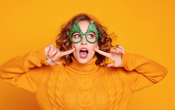 смешная веселая молодая женщина в глупых очках с рождественскими елками на ярко-желтой спинке - Фото, изображение