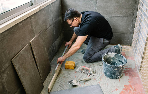Bricklayer vérifier le sol avec un niveau pour installer un plancher de tuiles - Photo, image