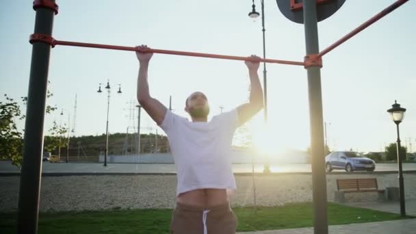 Homem jovem musculoso fazendo pull-ups na barra horizontal. Na área de treino perto de casa - Filmagem, Vídeo