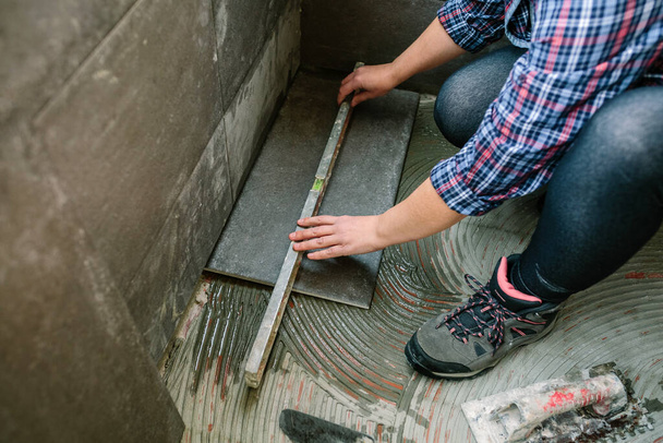 Nierozpoznawalny żeński murarz sprawdzający podłogę z poziomem umożliwiającym montaż podłogi dachówki - Zdjęcie, obraz
