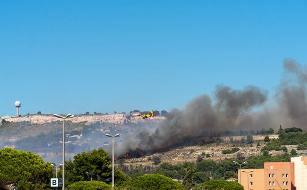 fuego comienza en las colinas de Marsella, cerca del aeropuerto de Marignane. avión amarillo de extinción de incendios va a tirar agua sobre él. - Foto, Imagen