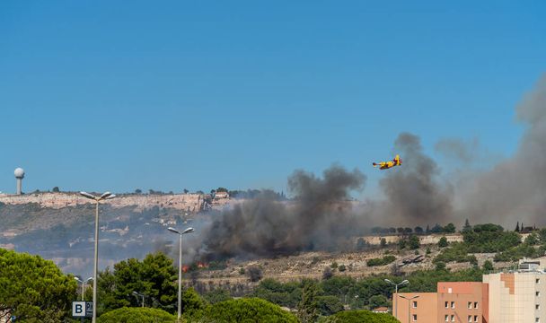 incêndio começa nas colinas de Marselha, perto do aeroporto de Marignane. O avião amarelo de combate a incêndios vai atirar água nele.. - Foto, Imagem