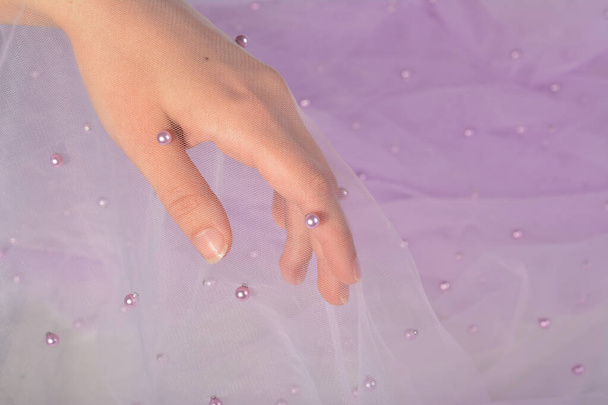 elegantní dámská ruka s fialovou elastickou tukovou tkaninou organza tylovou síťovinou s perlovými korálky. na šití svatebních a maškarních šatů. mezera pro text. - Fotografie, Obrázek