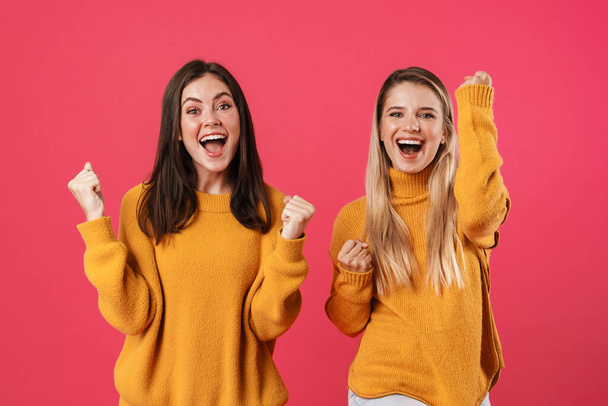 Image of excited beautiful women screaming and making winner gesture isolated over pink background - Foto, Imagen