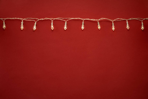 garland on red background, retro light bulbs burn with warm yellow light - Fotó, kép