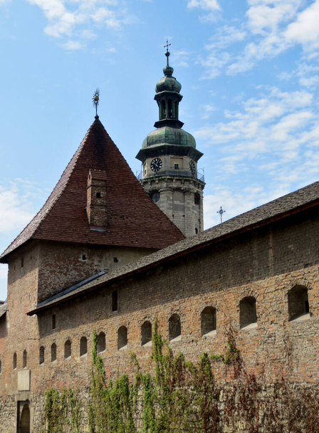 Fortress wall with a tower and a clock tower of the cathedral on a background of blue sky with clouds. Bernardine Church - Zdjęcie, obraz