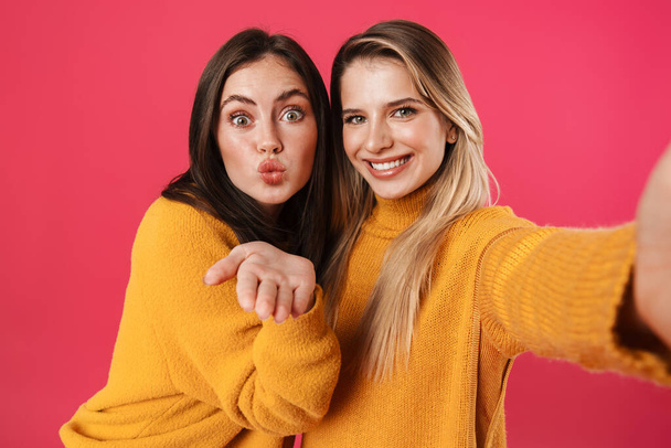 Image of happy beautiful women blowing air kiss while taking selfie isolated over pink background - Photo, Image