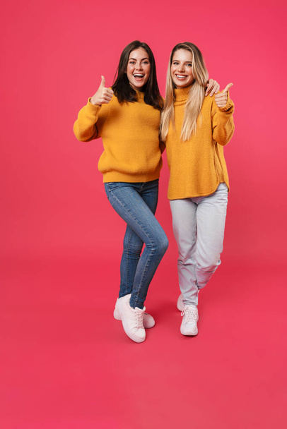 Image of cheerful caucasian women hugging and showing thumbs up isolated over pink background - Foto, imagen