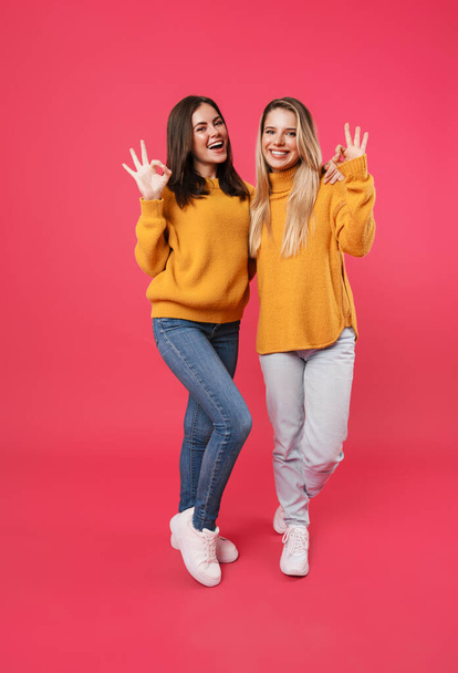 Image of cheerful caucasian women hugging and showing ok sign isolated over pink background - 写真・画像