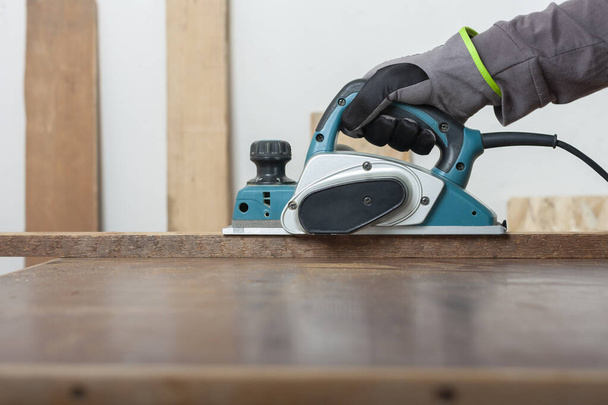 Плотник, работающий с электроагрегатом на деревянной доске на столе, на фоновой доске - Фото, изображение