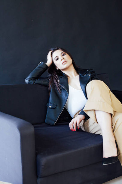 Beautiful fashionable brunette woman in a leather jacket on an office sofa - Fotoğraf, Görsel