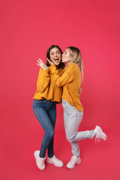 Full length portrait of two young female friends standing over pink background - Foto, afbeelding