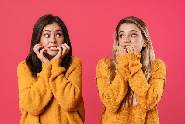 Image of scared caucasian women posing and looking at each other isolated over pink background - Foto, Imagem