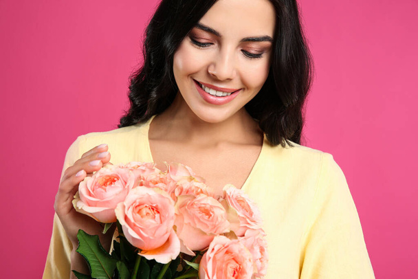 Portrait of smiling woman with beautiful bouquet on pink background - Fotó, kép