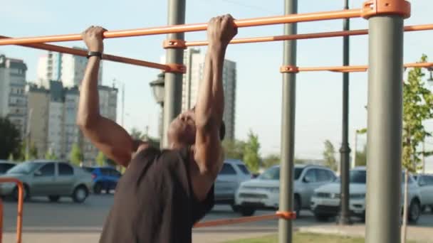 Κοντινό πλάνο του αφρικανού άνδρα κάνει ανάποδη λαβή pull-ups σε οριζόντια προπόνηση σε εξωτερικούς χώρους - Πλάνα, βίντεο