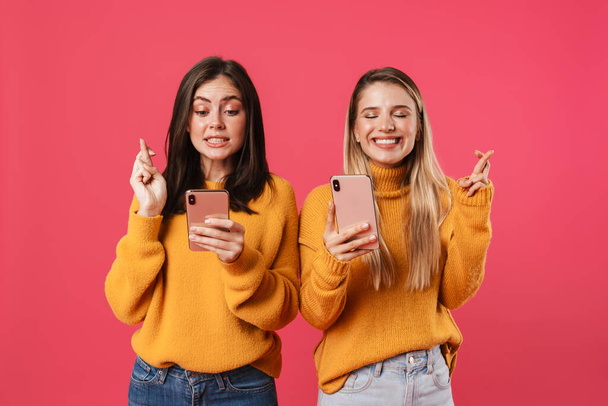 Image of pleased women using smartphones and holding fingers together isolated over pink background - Photo, image