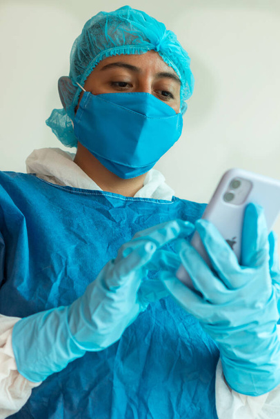 Médico femenino con mascarilla protectora en el hospital usando teléfono celular - Foto, Imagen