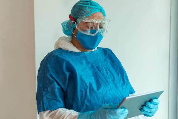 Portrait d'une femme médecin portant un masque médical avec une tablette numérique. Fond de mur clair, docteur lisant l'écriture en ligne. Portrait de spécialiste professionnel - Photo, image