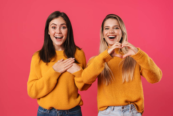 Image of joyful nice women showing heart gesture and holding hands on chest isolated over pink background - Fotó, kép