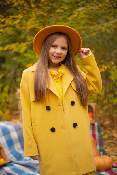 мила красива дівчина-підліток брюнетка в помаранчевому капелюсі, сукня і пальто поруч з осінніми прикрасами гарбузи, яблука, ковдри, сіно. Затишок
.  - Фото, зображення
