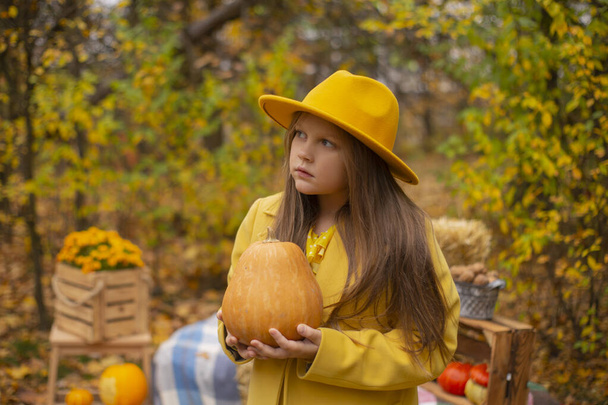 χαριτωμένο όμορφη έφηβη μελαχρινή κοπέλα σε ένα πορτοκαλί καπέλο, φόρεμα και παλτό κρατώντας μια κολοκύθα. Άνεση, φθινόπωρο. - Φωτογραφία, εικόνα