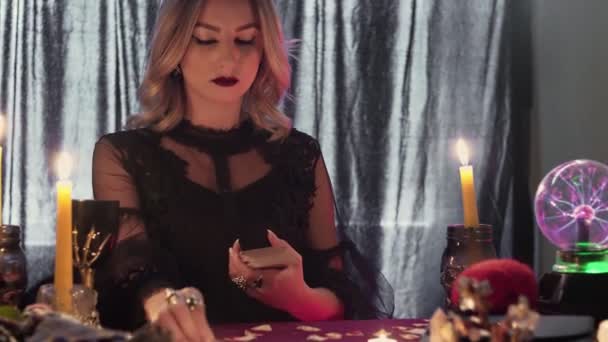 Mladý věštec u stolu ve světle svíček čte budoucnost na kartách v kouři - Záběry, video