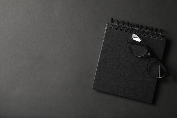 Glasses, notebook and space for text on dark background, top view. Black Friday concept - 写真・画像