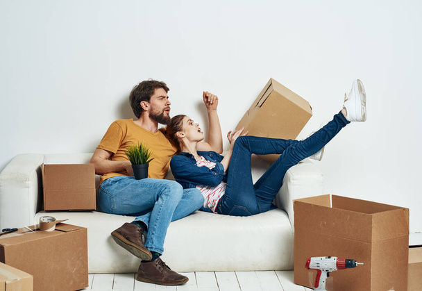 Ein Mann und eine Frau sitzen auf der Couch in der Nähe der Kisten mit Dingen, die das Innere des Raumes bewegen - Foto, Bild