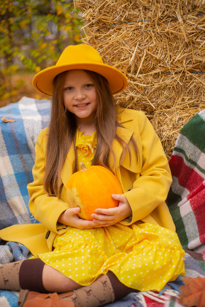 мила красива дівчина-підліток брюнетка в помаранчевому капелюсі, сукня і пальто, що тримає гарбуз. Затишок, осінь
. - Фото, зображення