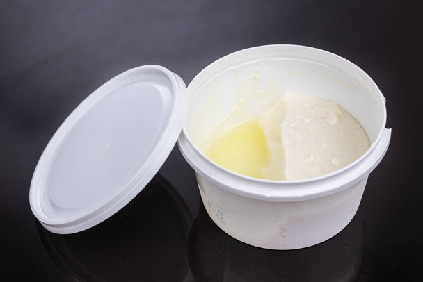 Lagen van wei-eiwit gevormd op de top van verpakte yoghurt na opening in donkere achtergrond. - Foto, afbeelding
